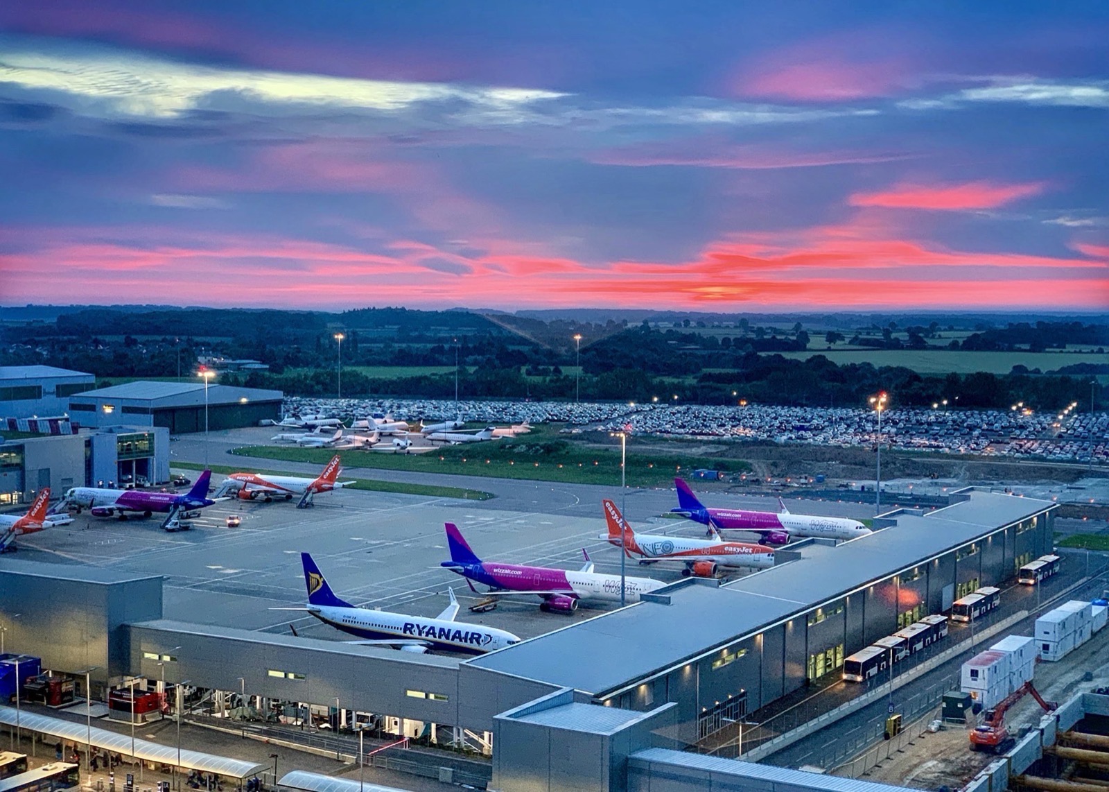 An airport apron at dusk, aircraft parked at the terminal under a red sky
