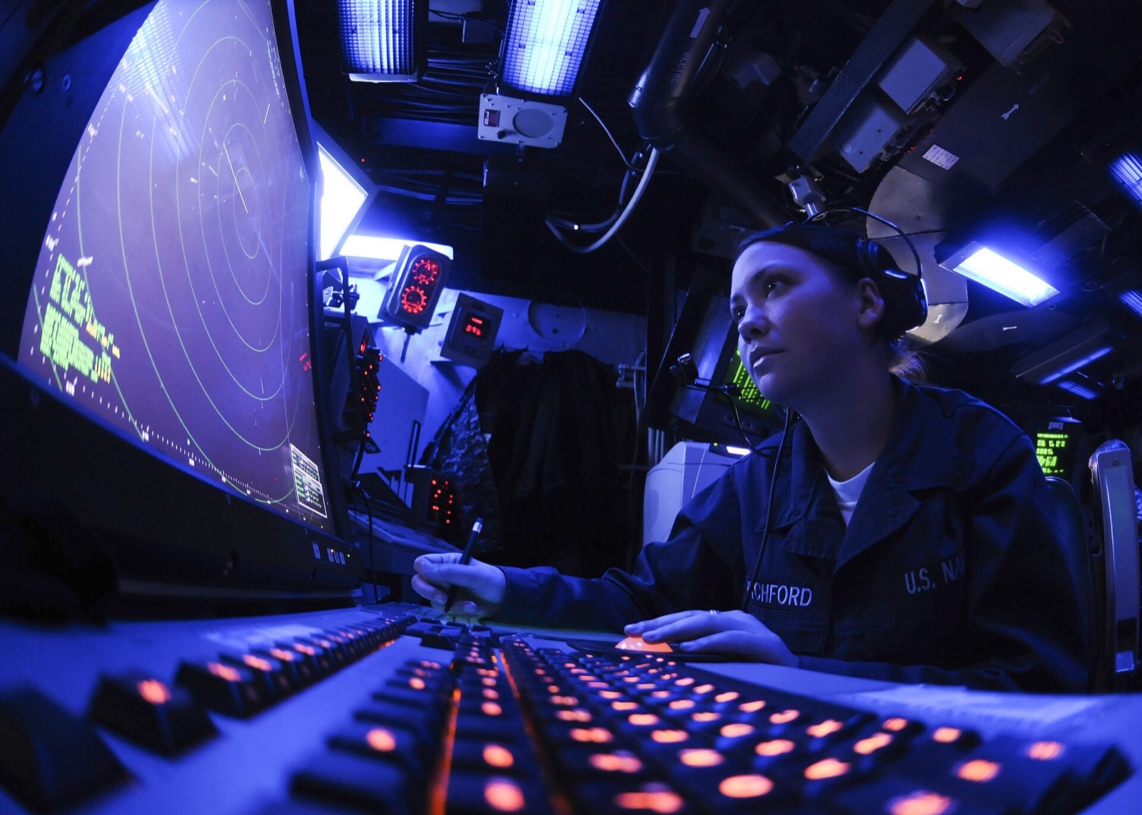A controller at a radar console in a darkened room, keyboard lit in amber
