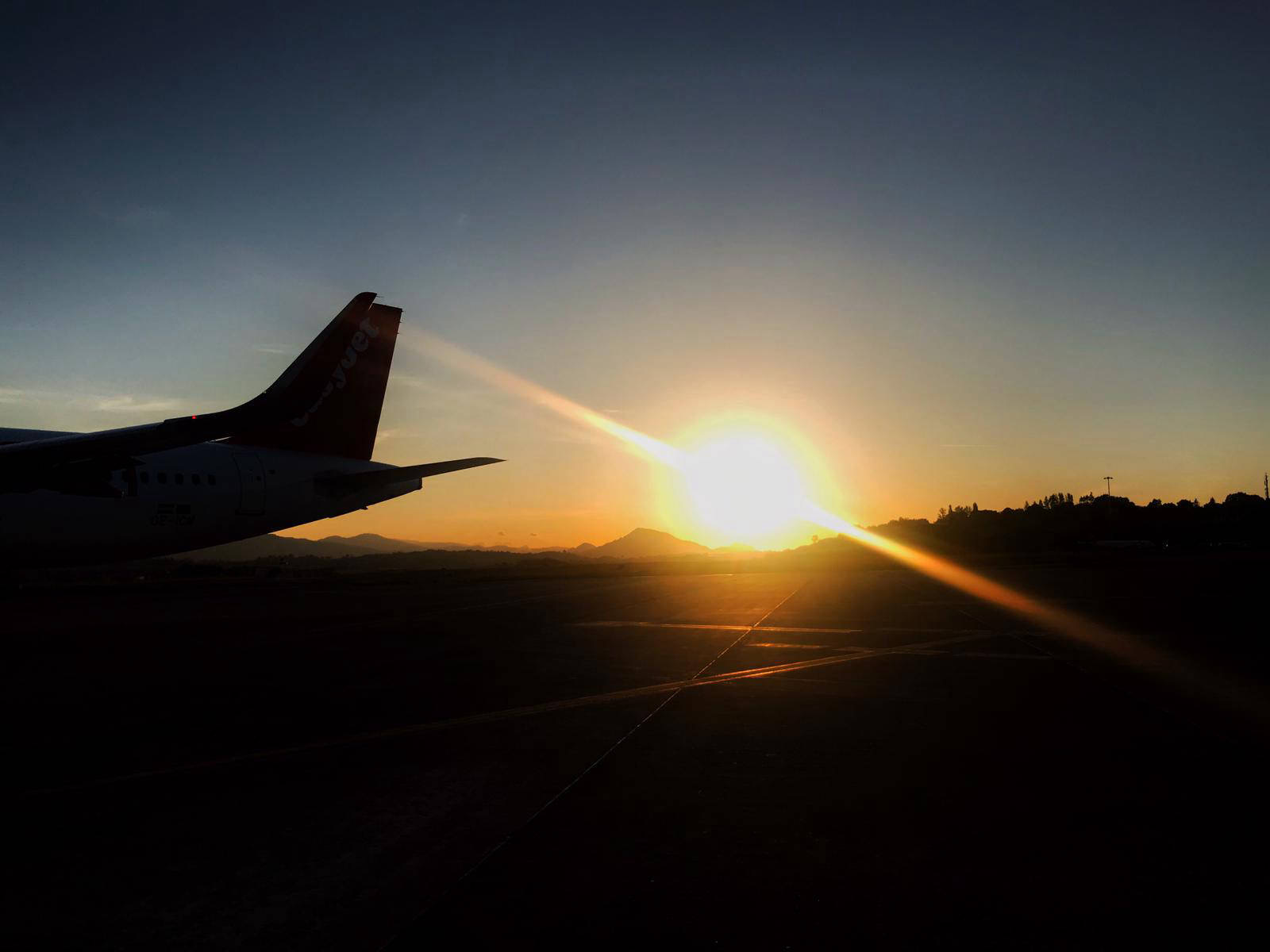 The tail of an aircraft against a low sun on the runway